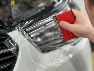 The process of installing a protective polyurethane film for paint on the front headlight of a car. PPF is a polyurethane film that helps protect glass and metal from scratches. Selective focus.  