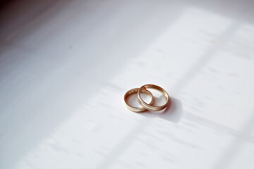 Two gold wedding rings are sitting on a white table. The rings are placed next to each other, and...