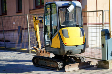 Small compact excavator parked on city street, tracked vehicle used for heavy construction work in an urban industrial setting. Tracked compact excavator parked in a downtown area close-up