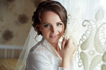 A woman is wearing a white dress and a veil. She is smiling and looking at the camera
