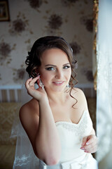 A woman is wearing a white dress and is wearing earrings. She is smiling and looking at the camera