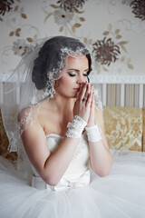 A woman in a wedding dress is praying. She is wearing a veil and a ring on her finger