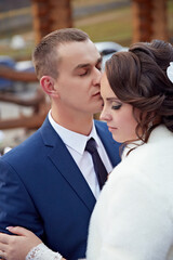 A man and woman are embracing each other in a blue suit and white fur coat. The man is wearing a tie and the woman is wearing a white fur coat. Scene is warm and affectionate