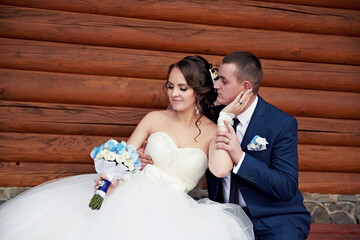 A bride and groom are sitting on a log, the bride is holding a bouquet and the groom is wearing a...