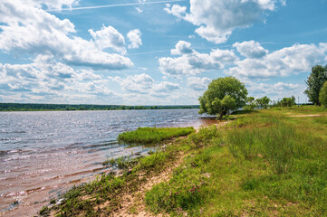 Landscape with river water's edge, far forest under blue sky with white clouds. Natural summer background.