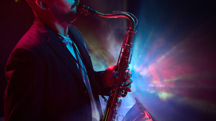 A musician is playing a saxophone under colorful stage lights in a dark moody setting enhanced by a smoke effect. Concept of live jazz performance atmosphere.