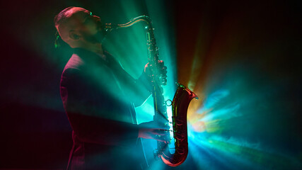 A musician is silhouetted while playing saxophone against vibrant stage lights in a dramatic...