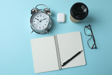 blank notepad with clock, alarm clock and pen on blue pastel pink background.