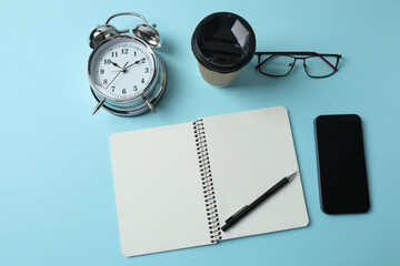 blank notepad with clock, alarm clock and pen on blue pastel pink background.