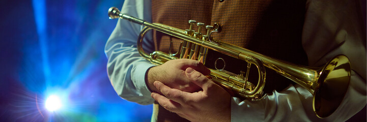 A musician confidently holds a trumpet while vibrant stage lights illuminate the background....