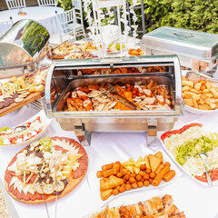 Rich buffet spread at an outdoor celebration with fried meat, cheese, cold cuts, salads, and...