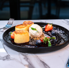 General view of syrniki dessert with ice cream, berry sauce and seasonal fruits