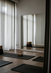 A yoga studio with black mats and stacked blocks, framed by soft translucent curtains and a large wall mirror reflecting the space. 