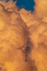 Massive orange thunderclouds illuminated by the evening sun with a deep blue sky peeking through. A dramatic natural scene capturing the power and beauty of the atmosphere.