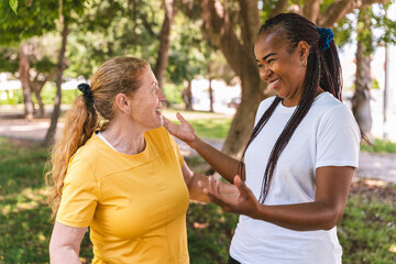 Diverse female friends conversing animatedly, smiling and gesturing while relaxing in sunny park setting