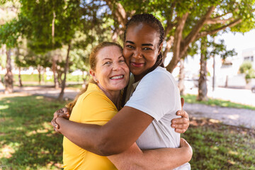 Mature and young women embracing warmly in park, sharing genuine bond across generations with...