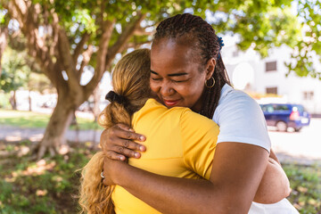 Multiracial friends hugging tightly, sharing genuine bond while standing in sunlit park with warm afternoon glow surrounding them