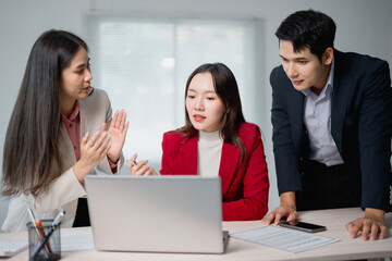 Three Asian businesspeople engaging in a work discussion around a laptop, collaborating on a...