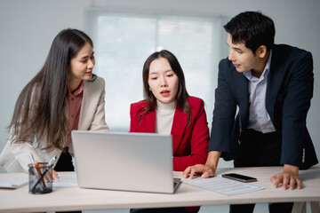 Fototapeta premium Three asian businesspeople discussing marketing strategy using laptop computer and analyzing financial statistics data on document at office desk, working together on a project