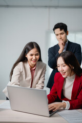 Three asian businesspeople are working together using a laptop in a brightly lit office meeting, discussing a project and collaborating on a task