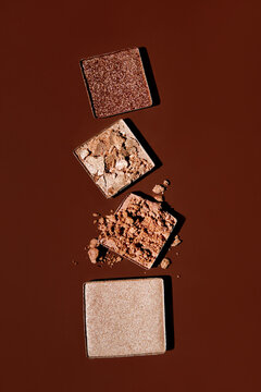 Top view of shattered bronze eye shadows on brown backdrop