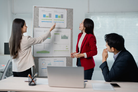 Businesswomen pointing at charts on whiteboard during a presentation to colleagues in the office meeting room, explaining company's financial performance and discussing new strategies