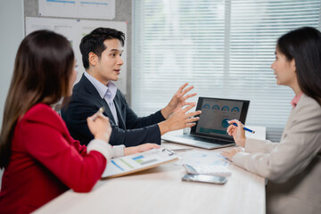 Marketing team discussing new sales pitch during a meeting in the office, using a laptop and analyzing financial data to develop a new marketing strategy
