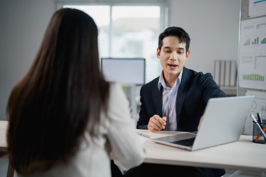 Asian businessman is showing something on a laptop to his female colleague during a meeting in a modern office, discussing about business strategy