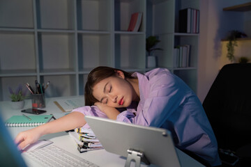 Working Late. Exhausted young woman resting her head on paperwork at her desk.