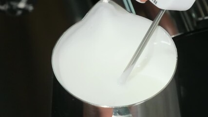 Female barista swirls milk in pitcher using mechanical mixer. Concept of coffee preparation using professional equipment slow motion