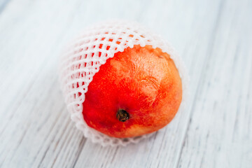 Fresh peach wrapped in protective netting on wooden surface