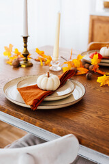 Decorative autumn table setting with white pumpkin and colorful leaves in cozy dining area