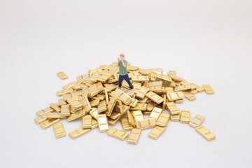 Miniature Person Standing Surrounded by Pile of Gold Bars