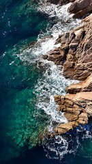 Vue a&eacute;rienne d&rsquo;une mer turquoise s&rsquo;&eacute;crasant sur des rochers en Corse, d&eacute;voilant la beaut&eacute; brute du littoral m&eacute;diterran&eacute;en et la transparence de l&rsquo;eau.