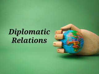Wooden hand grip the globe with the word Diplomatic Relations on a green background