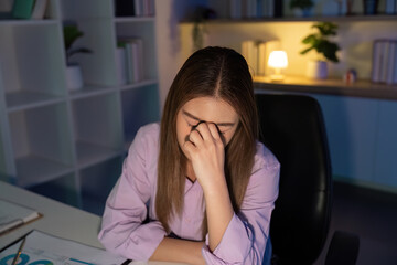 Working Late. Overwhelmed woman resting her head on her hand while staring at the computer.