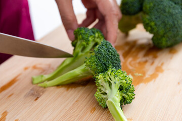 An Asian woman is cutting broccoli
