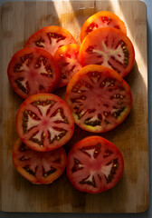 Vibrant heirloom tomato slices on a wooden cutting board, glistening under warm sunlight. 