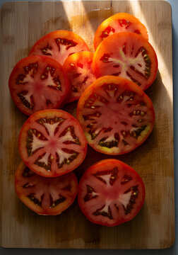 Vibrant heirloom tomato slices on a wooden cutting board, glistening under warm sunlight. 