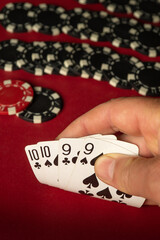A player examines a hand of poker cards showing two pairs, while various black and red casino chips...