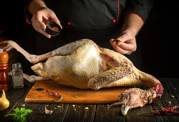 A chef expertly seasons a whole turkey on a wooden surface, with spices, herbs and tools placed...