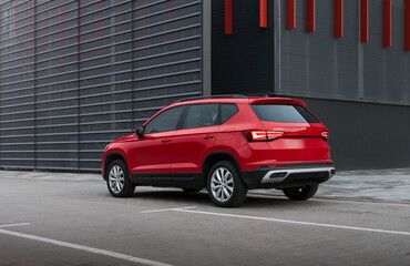 compact SUV in front of modern building. Three quarter rear view of red car crossover parked on city street. Car is parked on grey tiles