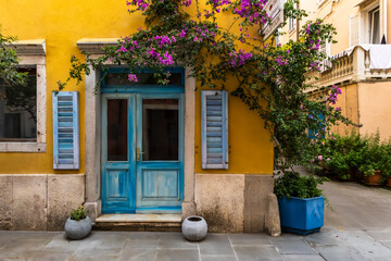 charming Mediterranean facade in contrast yellow and blue colors with colorful shutters and blooming flowers. traditional rustic architecture style. exterior