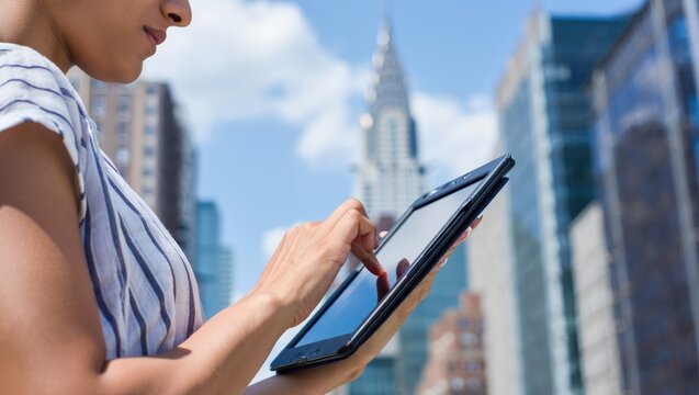 Woman using a tablet in New York City with the Chrysler Building visible.