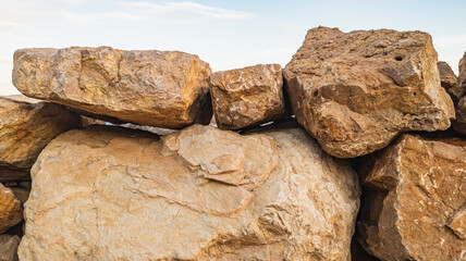 Natural sandstone blocks against a blue sky. Ancient beige stone. Wall stones for easy installation. Historical building materials, irregularly shaped. Rough mountain rocks for landscape project