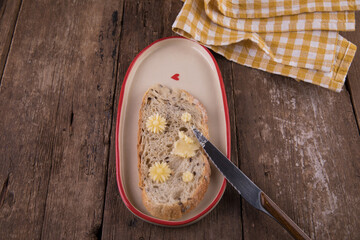 Butter in the form of flowers on a piece of bread on a plate on a wooden table.