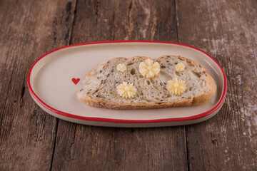 Butter in the form of flowers on a piece of bread on a plate on a wooden table.