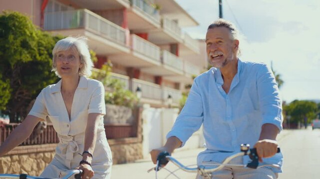 Retired couple sharing joyful moment while leaning on bicycles, laughing together during sunny day in peaceful suburban neighborhood, embodying love and active aging