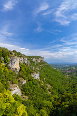 Naklejka premium Rocky cliffs dominating green valley in Autoire, France, under blue sky