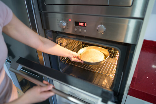 Woman placing focaccia dough into modern oven